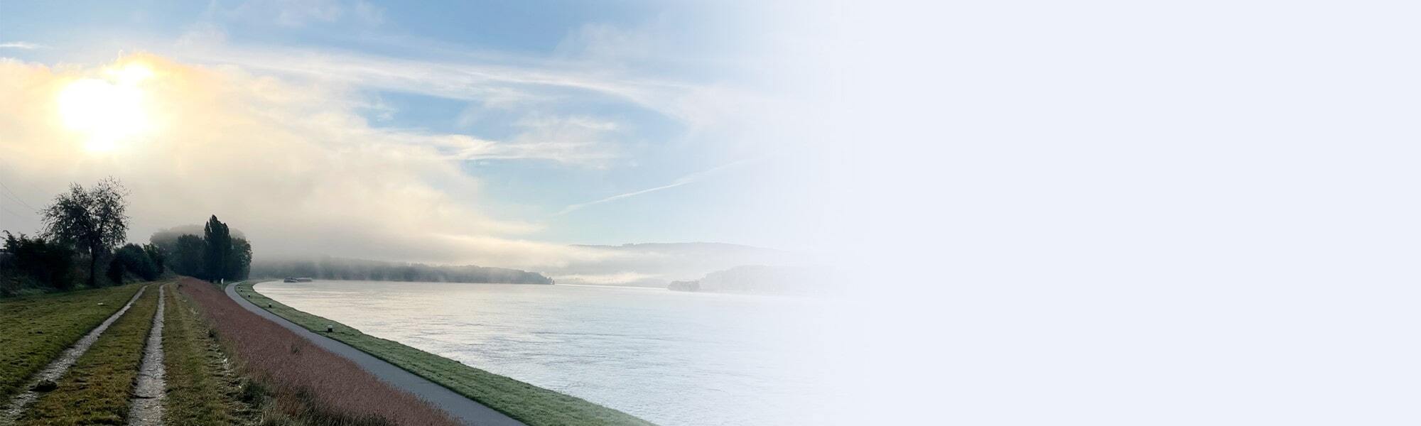 Nebliger Morgen an der Donau bei Krems, mit leichtem Sonnenlicht, Uferweg und ruhigem Flussverlauf